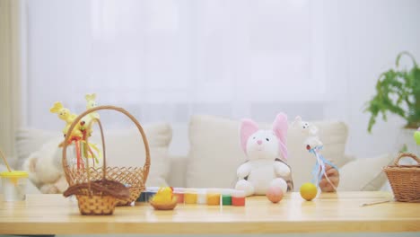 Little-jouful-girl-with-bunny-ears-on-his-head-is-playing-on-the-wooden-table,-full-of-Easter-decorations.-Girl-is-playing-with-Easter-bunnies-and-an-yellow-egg,-isolated.