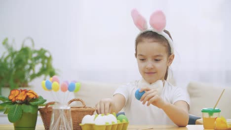 Pequeña-chica-linda-y-adorable-está-sonriendo-y-jugando-con-huevos-de-pollo-de-colores-en-sus-manos.-Concepto-vacaciones-de-Pascua.