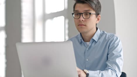 Male-student-sitting-against-bookshelf-and-using-laptop-in-the-library