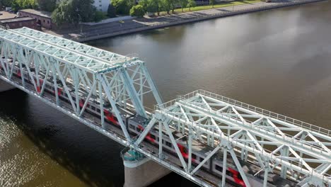 Luftaufnahme-der-Eisenbahnbrücke,-mit-einem-fahrenden-Zug-auf-ihr,-über-den-Fluss,-der-durch-eine-Großstadt-fließt