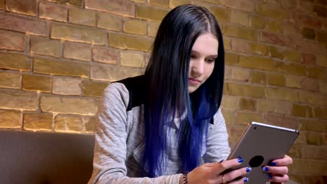 Closeup-shoot-of-young-pretty-caucasian-hipster-female-with-dyed-hair-texting-on-the-tablet-and-smiling-in-a-cozy-apartment-indoors