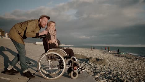 Man-is-hugging-his-wife-sitting-in-invalid-carriage-on-sea-embankment