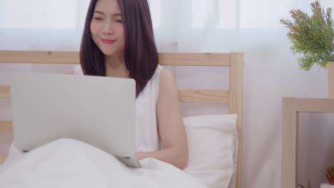 Young-business-freelance-Asian-woman-working-on-laptop-checking-social-media-while-lying-on-the-bed-when-relax-in-bedroom-at-home.-Lifestyle-women-at-house-concept.