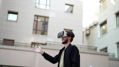 Panning-Zeitlupe-Aufnahme-von-jungen-Mann-in-vr-Brille-im-Freien-in-der-Stadtstraße-stehen-und-die-Erforschung-von-Daten-in-der-virtuellen-Realität-visualisiert.-Mann-wischen-und-vergrößern-Info