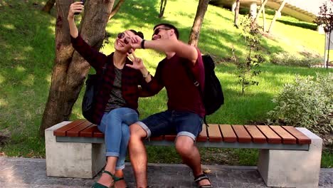 Una-joven-pareja-enamorada-es-fotografiada-sentada-en-un-banco-en-el-parque.-Sonríen-y-se-abrazan.