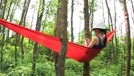 Mujer-relajándose-en-hamaca-con-teléfono-inteligente-en-la-selva-tropical,4k