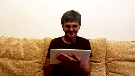 Attractive-adult-woman-working-on-her-tablet-while-sitting-on-a-sofa-at-home.