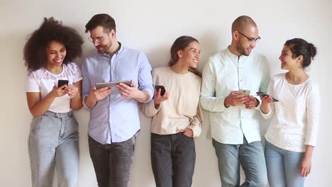 Happy-diverse-young-friends-stand-in-row-talk-use-phones