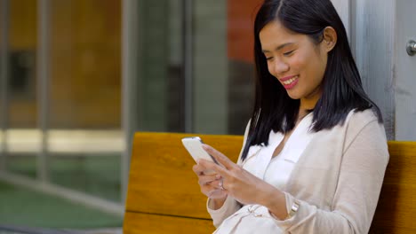 asiatische-Frau-mit-Smartphone-auf-der-Bank-sitzen