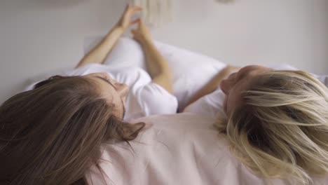 Close-up-of-happy-young-women-emotionally-chatting-while-laying-on-the-bed