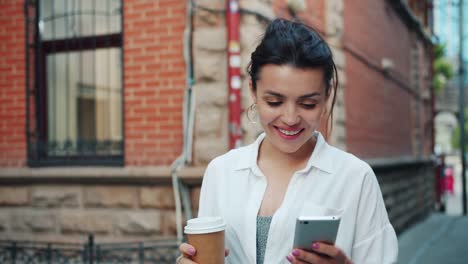 Slow-motion-of-beautiful-lady-using-smartphone-holding-coffee-walking-smiling