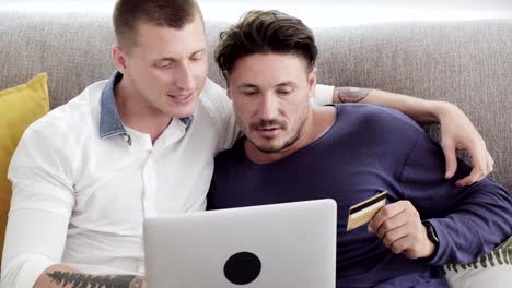 Gay-couple-relaxing-on-couch-using-laptop-computer.-Completing-online-shopping.