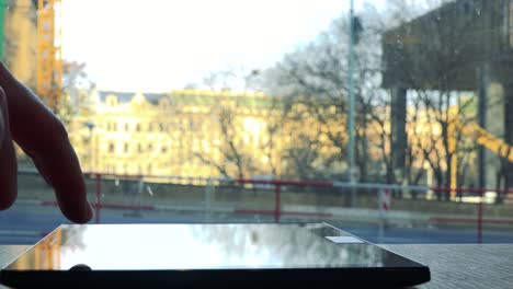 A-woman-works-on-a-tablet-laid-on-a-table-in-a-cafe---closeup-on-the-phone,-a-window-in-the-background