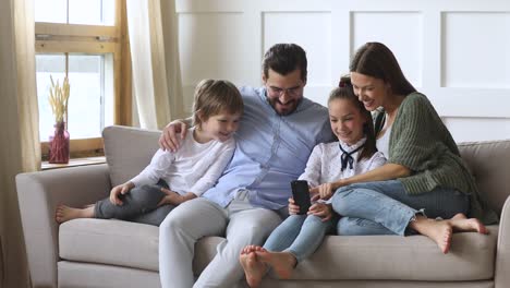 Glückliche-Eltern-mit-Kindern-entspannen-auf-dem-Sofa-mit-Smartphone-Apps