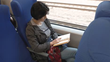 una-mujer-de-tamaño-mediano-se-sienta-en-un-tren.-Lee-un-libro.