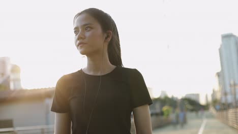 Beautiful-asian-woman-athlete-running-resting-exhausted-after-a-cardio-workout-exercise-in-the-urban-city-sunset.-Jogging-lifestyle-healthy.-Girl-runner-wearing-earphones-listening-to-music.