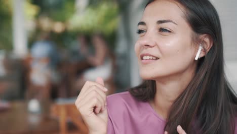 Young-woman-puts-on-wireless-earphones,-listens-to-music-and-dances-in-cafe