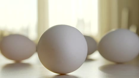 Four-chicken-eggs-on-the-table-in-a-sunny-kitchen,-one-egg-is-rotated