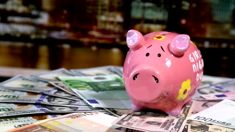 Pink-piggy-bank-on-rotating-surface-with-dollars-and-euro-banknotes.