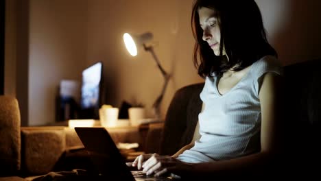 Young-concentrated-woman-using-laptop-computer-and-typing-message-at-home-in-night-time