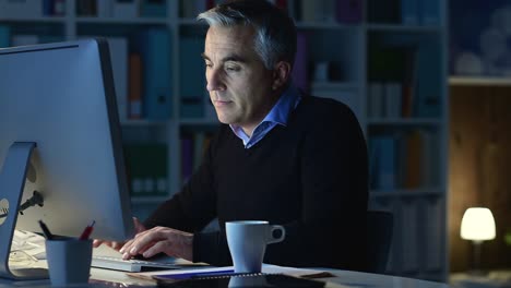 Smiling-man-working-with-his-computer-late-at-night