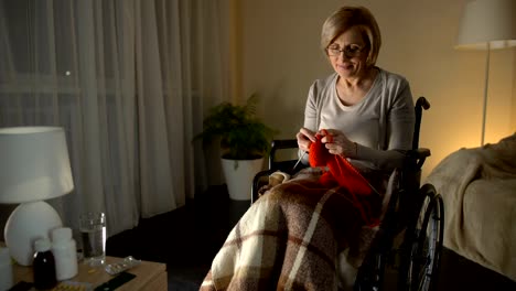 Cheerful-old-woman-sitting-in-wheelchair-knitting-scarf,-taking-care-of-children