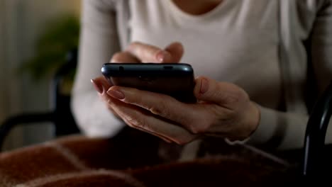 Old-lady-in-wheelchair-scrolling-webpage-checking-weather-forecast-on-smartphone