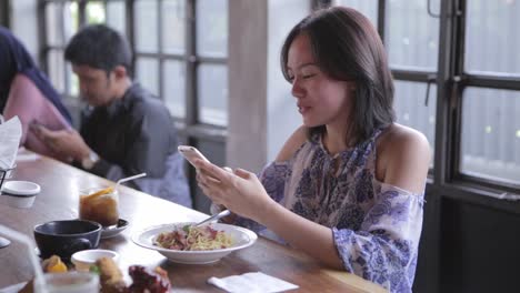 Mujer-está-comprobando-su-teléfono-mientras-comen-almuerzo-con-amigos-en-el-restaurante