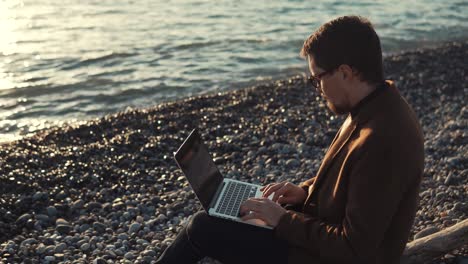 Geschäftsmann-arbeitet-abends-am-Meer-mit-Laptop-und-internet