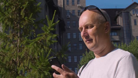 Adult-man-in-sunglasses-texting-in-chat-on-smartphone-in-city