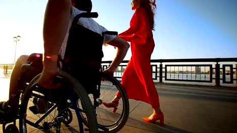 Chico-paseos-en-silla-de-ruedas-y-una-hermosa-muchacha-camina-con-él-en-el-muelle-al-atardecer