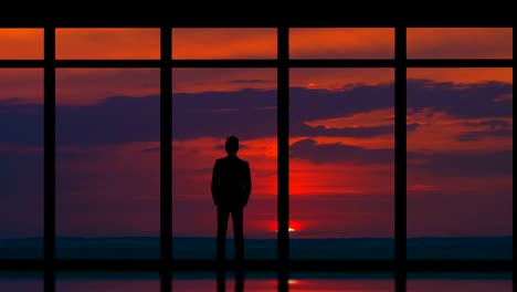 The-man-standing-near-panoramic-windows-on-the-sunset-background.-time-lapse