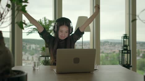 Young-Asian-woman-typing-on-laptop-while-listening-to-music-over-headphones