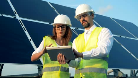 Zwei-Arbeiter-Stand-in-der-Nähe-von-Sonnenkollektoren-mit-einer-Tablette-hautnah.