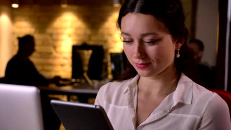 Closeup-of-young-caucasian-female-office-worker-using-the-tablet-getting-surprised-and-smiling-on-the-workplace-indoors