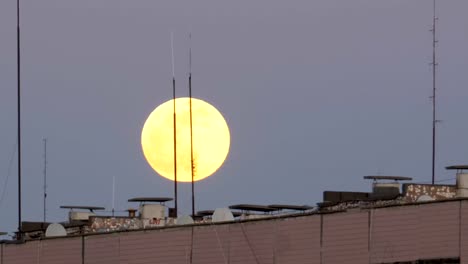 La-gran-luna-llena-sobre-el-tejado-de-un-edificio-Multistory-se-está-moviendo-hacia-arriba