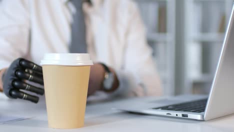 Businessman-with-Prosthetic-Arm-Typing-on-Laptop-and-Drinking-Coffee