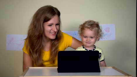 Young-woman-with-her-child-girl-looking-funny-cartoons-on-tablet-computer.