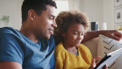 Padre-y-su-hija-pre-adolescente-relajarse-en-el-sofá-usando-la-computadora-de-la-tableta,-de-cerca