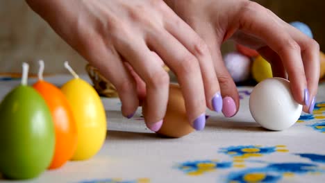 Happy-Easter.-female-hands-take-off-the-table-two-easter-eggs.-colorful-candles-and-colorful-Easter-eggs-in-the-background.