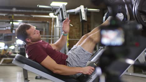 Fitness-Trainer-Lying-on-Leg-Press-Machine-and-Speaking-on-Camera