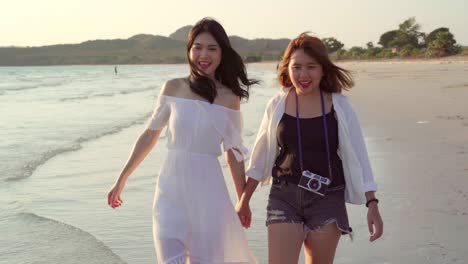 Young-Asian-lesbian-couple-walking-on-beach.-Beautiful-women-friends-happy-relax-walking-on-beach-near-sea-when-sunset-in-evening.-Lifestyle-lesbian-couple-travel-on-beach-concept.