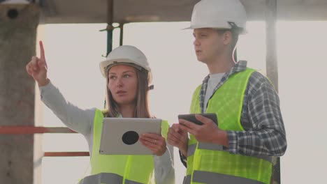 Engineers-designers-stand-on-the-roof-of-the-building-under-construction-and-discuss-the-plan-and-the-progress-of-construction-using-a-tablet-and-mobile-phone