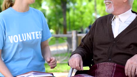 Sincere-social-worker-reading-book-to-disabled-pensioner-in-park,-volunteering