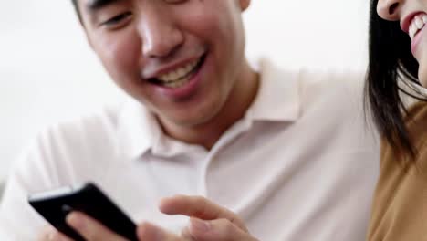 Close-up-Asian-couple-using-smartphone-browsing-social-media-communication-and-shopping-online-while-sitting-on-the-sofa-at-home.