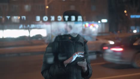 Joven-mujer-navegando-por-Internet-en-la-almohadilla-cuando-espera-el-autobús-en-la-ciudad-de-la-noche