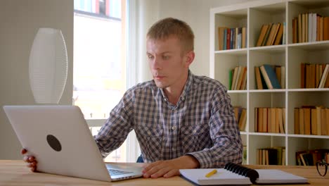 Caucasian-businessman-talking-in-videochat-using-laptop-on-bookshelves-background.