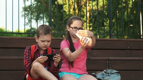 Die-ältere-Schwester-und-der-Bruder-sitzen-auf-der-Straße-und-schauen-auf-Smartphones.