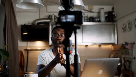 Happy-young-African-travel-blogger-man-talks-recording-video-for-blog-with-professional-camera-at-home-slow-motion.