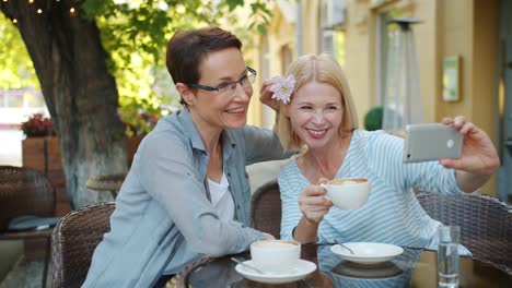 Glückliche-Freunde-machen-Selfie-im-Café-mit-Smartphone-dekorieren-Haar-mit-Blume